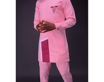 May include: A light pink two-piece outfit. The long-sleeved top has a small pocket with a burgundy accent and a decorative design. The trousers are a matching light pink colour. The outfit has a modern, tailored design.
