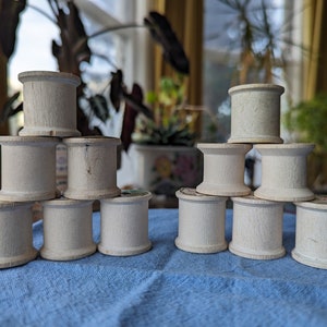 May include: A stack of wooden spools arranged in a pyramid shape. The spools are white and have a natural wood grain. There are two stacks of spools, each with five spools.