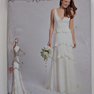 May include: A Simplicity sewing pattern envelope 3596 by Leanne Marshall featuring two dress designs. View A is a white sleeveless floor-length gown with tiered ruffles and a V-neckline. View B is a long-sleeved gown with a V-neck and lace detailing.