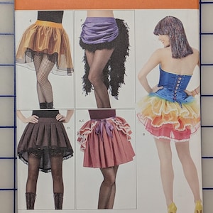 May include: Simplicity sewing pattern 1346 H5 for skirts in sizes 6, 8, 10, 12, 14. The envelope displays five variations of skirts, including a gold layered skirt, a purple skirt with black feathers, a brown pleated skirt, a pink skirt, and a rainbow tutu.