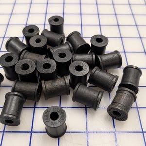 May include: A collection of small, cylindrical black wooden spools with a central hole. Each spool features text printed on the top edge that reads 10 YARDS 10 YARDAS. The spools are arranged in a cluster, showing their dark, textured wood grain finish.