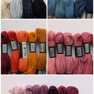May include: A collection of multi-colored yarn skeins arranged in rows. Each skein features a paper label with printed identification numbers and text including ECRU, NOIR, and various numerical codes. The yarn colors include cream, gray, navy, black, blue, orange, yellow, pink, and purple shades.