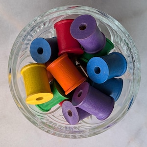 May include: A glass bowl filled with colorful wooden spools in shades of red, orange, yellow, green, blue, and purple.