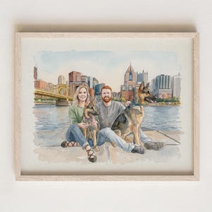 May include: A watercolor illustration in a light wood frame depicting a person with blonde hair and a person with a red beard sitting by a river with two German Shepherd dogs. The background features a city skyline with a yellow bridge.