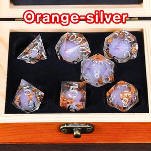 May include: A set of seven iridescent dice with orange and silver flecks in a wooden box. The dice are numbered 1 through 6 and 20. The box has a latch and is labelled "Orange-Silver".