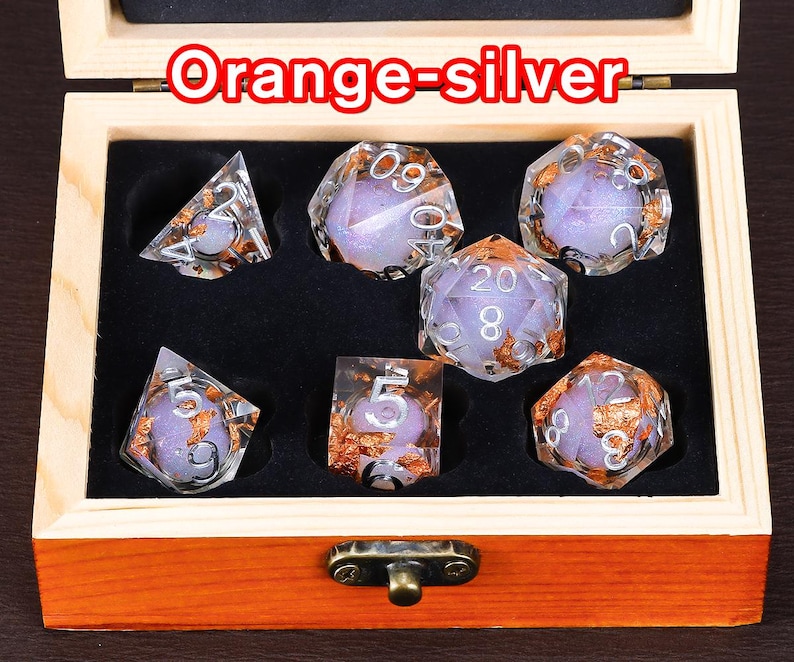 May include: A set of seven iridescent dice with orange and silver flecks in a wooden box. The dice are numbered 1 through 6 and 20. The box has a latch and is labelled "Orange-Silver".