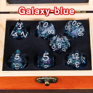 May include: A set of seven galaxy-blue dice with silver numbers in a wooden box. The dice are in a variety of shapes and sizes, including a d4, d6, d8, d10, d%, d12, and d20.