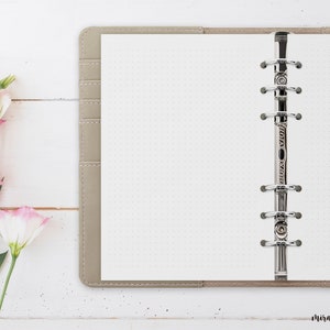 Könnte beinhalten: Ein beigefarbenes, ledergebundenes Journal mit einem silbernen Ringbinder und weißen, gepunkteten Seiten.