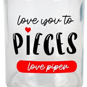 May include: A clear glass jar with a silver lid. The jar has a red and black design that says "love you to pieces" with a red heart and the words "love pipen" in red.