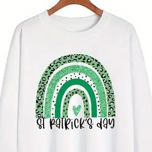 May include: White sweatshirt with a green rainbow design and the text "St. Patrick's Day".