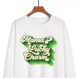May include: White long-sleeve sweatshirt with a green and white graphic print that says "Mama's Lucky Charm" in a retro font.
