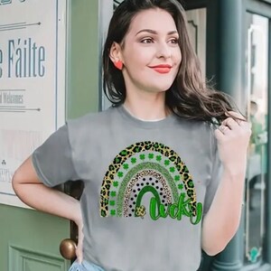 May include: A gray t-shirt with a green, black, and gold rainbow design and the word "lucky" in green. The rainbow is made up of different patterns, including leopard print, polka dots, and shamrocks.