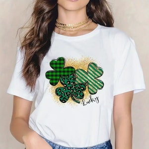 May include: White t-shirt with a green, black, and gold shamrock design and the word "Lucky" printed on the front.