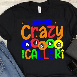 May include: Black t-shirt with the text "Crazy Bingo Caller!" in colorful letters. The text is surrounded by colorful bingo balls.