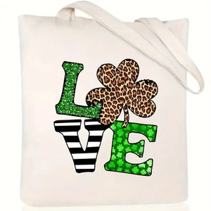 May include: A white canvas tote bag with a green, black, and brown "LOVE" design. The "L" is green glitter, the "O" is a brown and black leopard print shamrock, the "V" is black and white stripes, and the "E" is green glitter with small shamrocks.
