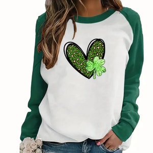 May include: White long-sleeve shirt with green raglan sleeves. The shirt features a green heart with a shamrock design.