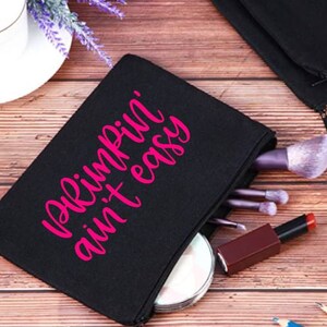 May include: Black canvas makeup bag with a pink zipper and the text "Pimpin' ain't easy" in pink.