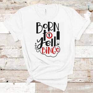 May include: White t-shirt with black text that reads "Born to yell Bingo" with a red circle with the number 1 inside.