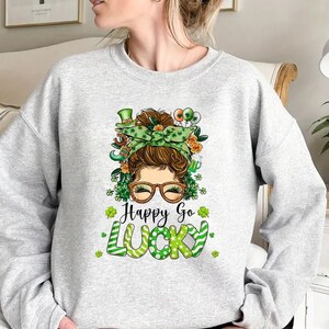 May include: A gray sweatshirt with a green, white, and gold graphic of a woman with a shamrock headband and the text "Happy Go Lucky".