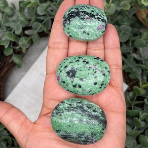 Może przedstawiać: Trzy zielone, czarne i różowe zoisity w kształcie kamieni polerowanych. Kamienie są gładkie i wypolerowane, ułożone w rzędzie od największego do najmniejszego.