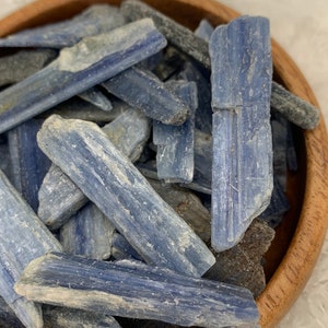 May include: A bowl filled with blue kyanite crystal points. The crystals are a light blue color and have a rough, natural texture.