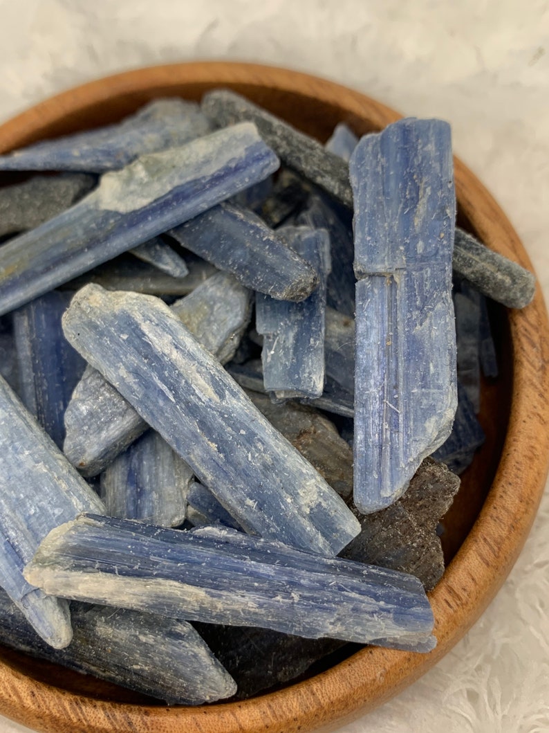May include: A bowl filled with blue kyanite crystal points. The crystals are a light blue color and have a rough, natural texture.