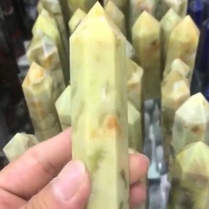 May include: A collection of green and white crystal points, also known as wands, with a unique marbled pattern. The points are displayed on a table, with one being held in a hand.