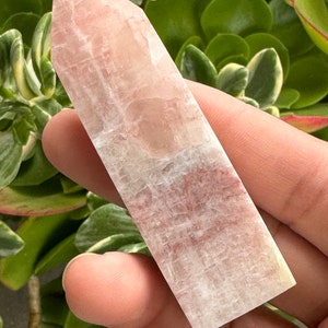 May include: A clear, white, and pink crystal point with a smooth, polished surface. The crystal is shaped like a long, thin pyramid.