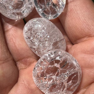 May include: Four clear quartz crystal tumbled stones with a crackled surface. The stones are smooth and polished.