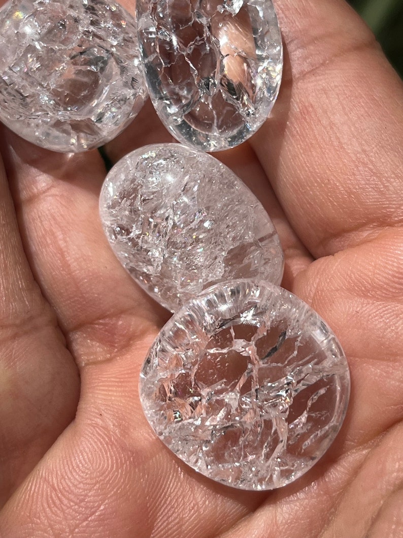May include: Four clear quartz crystal tumbled stones with a crackled surface. The stones are smooth and polished.