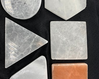 May include: Six coasters made of white selenite, with one coaster made of orange selenite. The coasters are in various shapes, including round, square, triangular, and hexagonal.