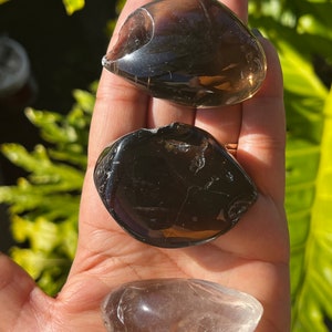 May include: Three tumbled stones, one clear quartz, one smoky quartz, and one black obsidian. The stones are smooth and polished.