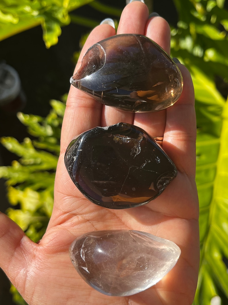 May include: Three tumbled stones, one clear quartz, one smoky quartz, and one black obsidian. The stones are smooth and polished.