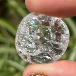 May include: A clear quartz crystal with a cloudy, iridescent appearance. The crystal is oval shaped and has a smooth, polished surface.