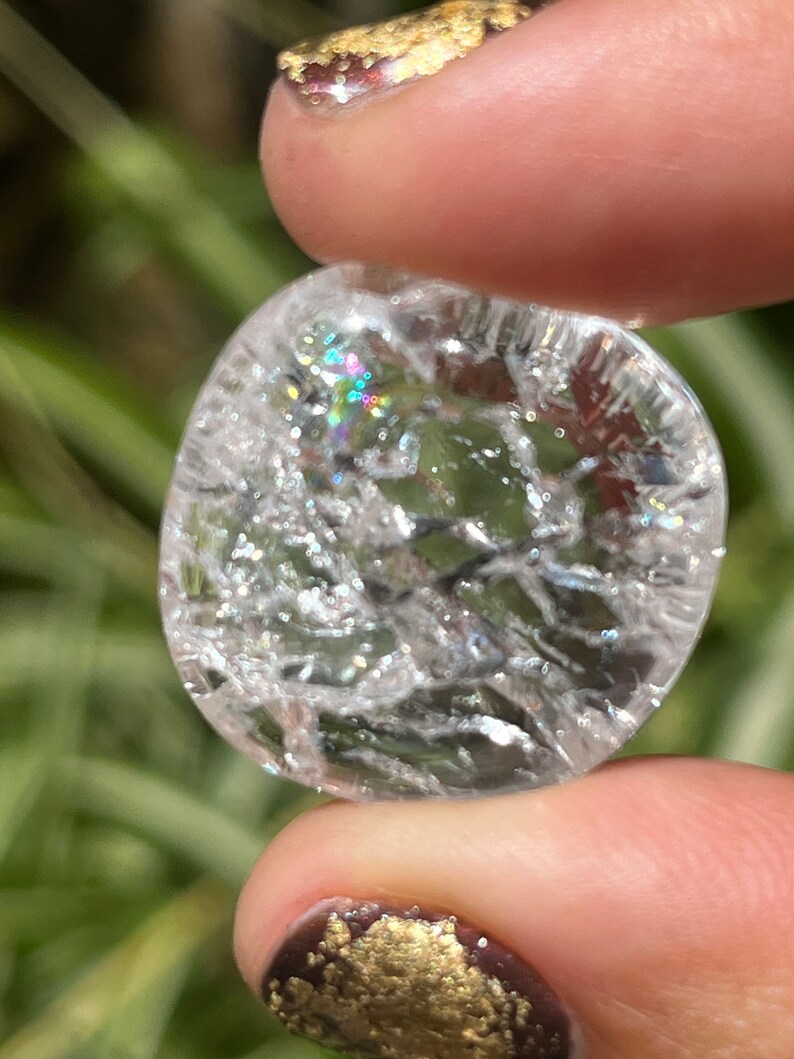 May include: A clear quartz crystal with a cloudy, iridescent appearance. The crystal is oval shaped and has a smooth, polished surface.