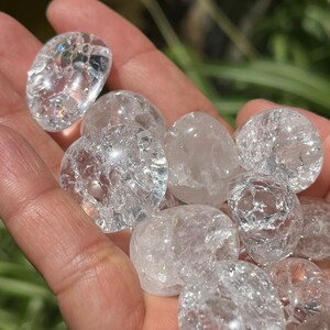 May include: A collection of clear quartz tumbled stones with a cloudy, milky appearance. The stones are smooth and polished, with a variety of sizes and shapes.