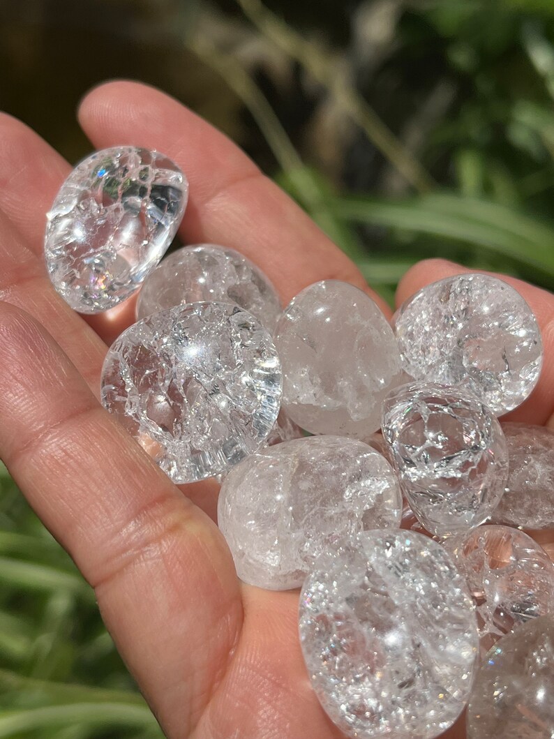 May include: A collection of clear quartz tumbled stones with a cloudy, milky appearance. The stones are smooth and polished, with a variety of sizes and shapes.