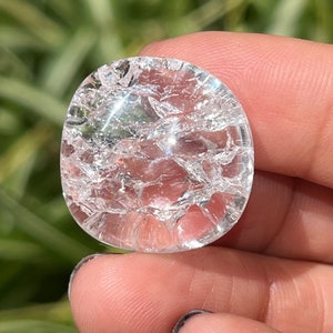 May include: A clear quartz crystal with a cracked surface. The crystal is round and has a smooth, polished finish.