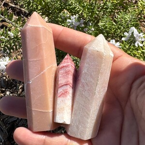 May include: Three polished crystal points in shades of pink, white, and red. The points are smooth and have a natural, organic look.
