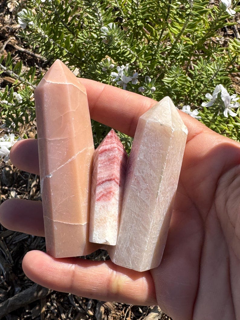 May include: Three polished crystal points in shades of pink, white, and red. The points are smooth and have a natural, organic look.