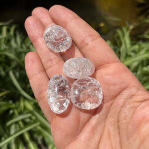 May include: Four clear quartz crystal tumbled stones with a rough, textured surface. The stones are oval shaped and have a translucent appearance.
