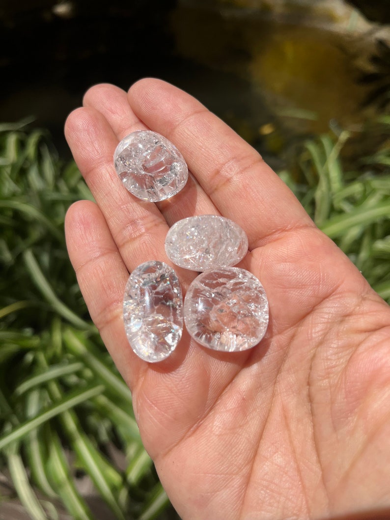May include: Four clear quartz crystal tumbled stones with a rough, textured surface. The stones are oval shaped and have a translucent appearance.