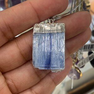 May include: A silver pendant with a light blue, rectangular, striated gemstone. The gemstone is set in a silver frame.