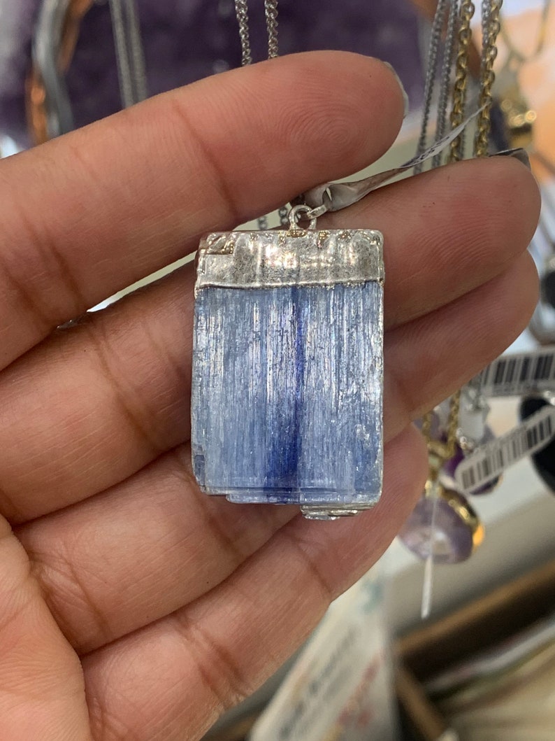 May include: A silver pendant with a light blue, rectangular, striated gemstone. The gemstone is set in a silver frame.