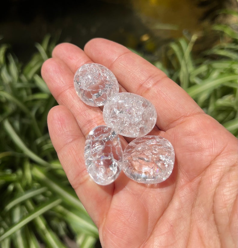 May include: Four clear quartz crystal tumbled stones with a rough, textured surface. The stones are oval shaped and have a translucent appearance.