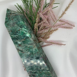 May include: A green and brown crystal point with a smooth, polished surface. The crystal is shaped like a long, thin pyramid.