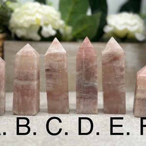May include: Six pink and white striped crystal points, labeled A through F, arranged in a row on a table.