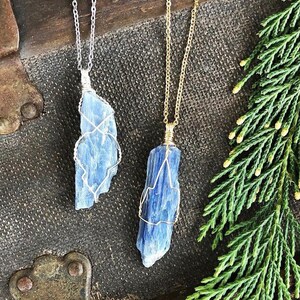 May include: Two blue kyanite crystal pendants on silver and gold chains. The crystals are wrapped in wire and have a natural, raw look.