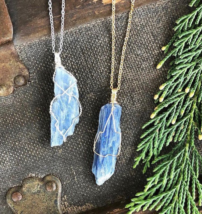 May include: Two blue kyanite crystal pendants on silver and gold chains. The crystals are wrapped in wire and have a natural, raw look.