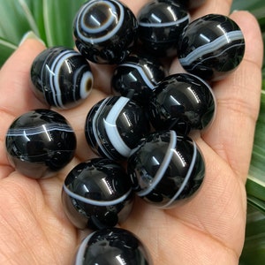 May include: A collection of black and white agate spheres. Each polished stone features unique banding patterns in white against a glossy black surface. The spheres vary in size and pattern, creating a visually appealing display.